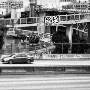 Black and white photo of a banner found hanging above the highway in Portland Oregon. The banner says “ATLANTA, PORTLAND STANDS IN SOLIDARITY”