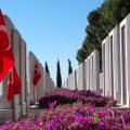 A flag of Turkey on a stand outside surrounded by pink flowers in a courtyard